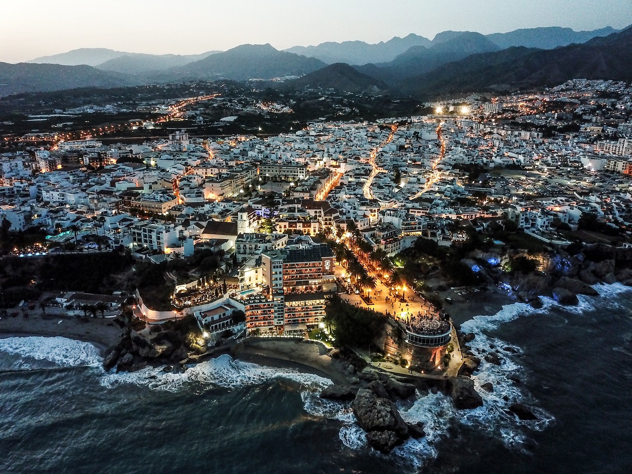 Malaga travel guide: Aerial night view of Málaga’s illuminated coastal cityscape along the Mediterranean Sea.