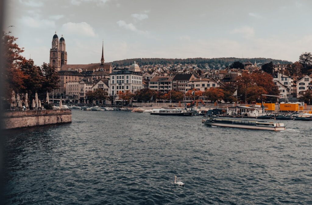 A scenic view of Zurich’s Old Town along the Limmat River, showcasing historic buildings, churches, and boats on the water.