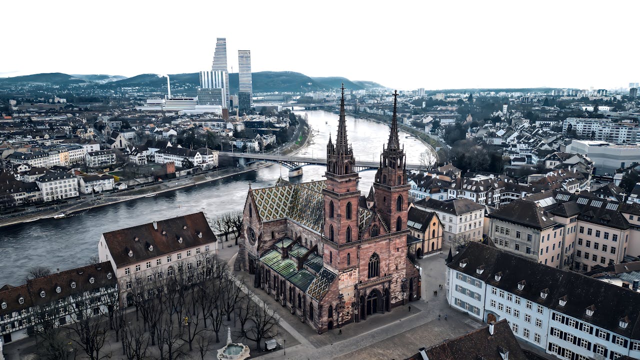 Aerial view of Basel Cathedral with the Rhine River flowing through Basel, Switzerland, highlighting the city's blend of historic architecture and modern skyline.