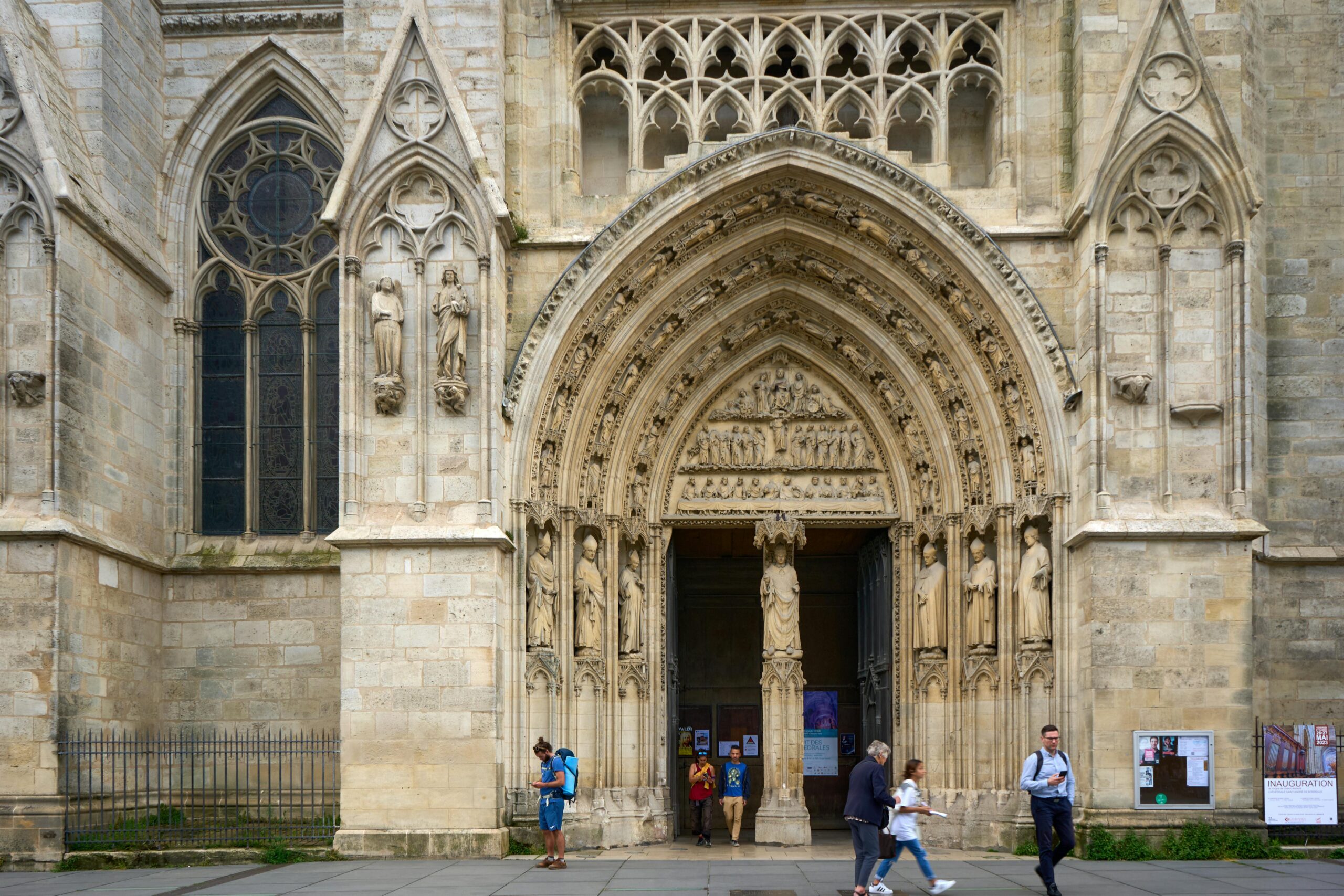 المدخل القوطي المعقد لكاتدرائية بوردو (Cathédrale Saint-André)، يعرض النقوش الحجرية والمنحوتات التفصيلية مع مرور الزوار بجانبه.